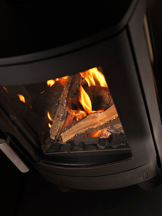 Close-up of a black gas stove with a glass door showing glowing orange flames and logs inside.